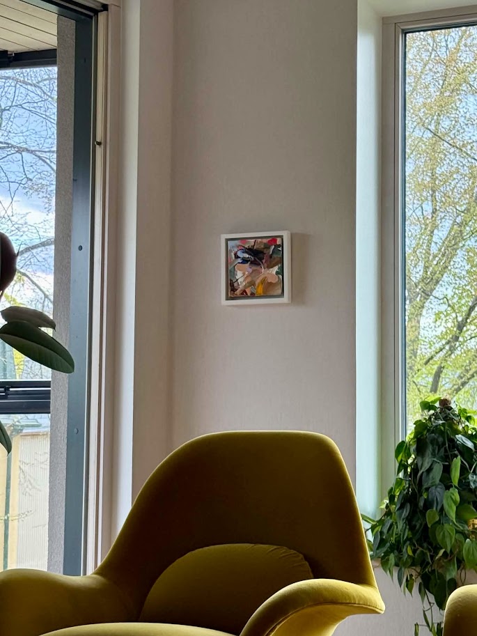 Small abstract painting on wall between windows with yellow chair and plants